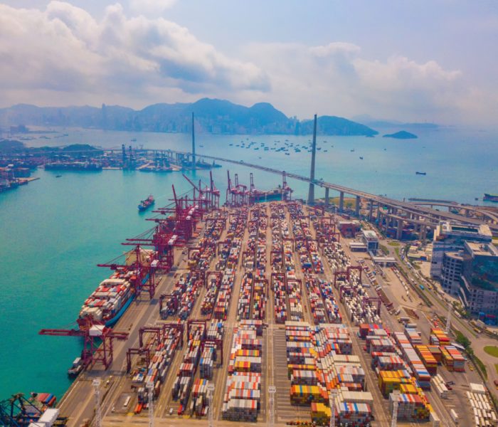 Aerial top view of container cargo ship in the export and import business and logistics international goods in urban city. Shipping to the harbor by crane in Victoria Harbour, Hong Kong.